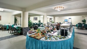 A buffet setup with various food items and a large pot, surrounded by tables and chairs in a spacious room with a chandelier. - Hotel Purbani International Limited (Dhaka)