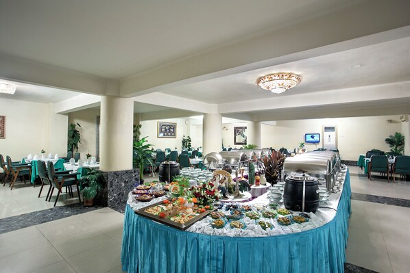 A buffet setup with various food items and a large pot, surrounded by tables and chairs in a spacious room with a chandelier. - Hotel Purbani International Limited (Dhaka)