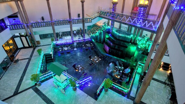 A multi-level atrium with a central open space surrounded by tables and chairs, wooden pillars, and decorative lighting. - Hotel Purbani International Limited (Dhaka)
