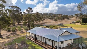 A modern house with a metal roof, surrounded by a grassy area and trees. - Merilli1885 - Private, Luxury Cottage (Currency Creek)