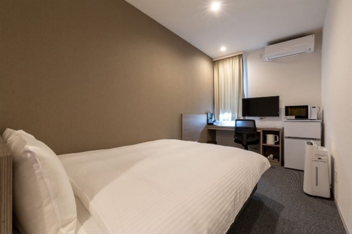 Ett hotellrum med en säng, ett skrivbord med en dator, en tv och en luftkonditioneringsanläggning.