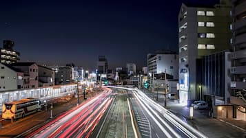 A nighttime cityscape with illuminated buildings and a busy street with light trails from moving vehicles.