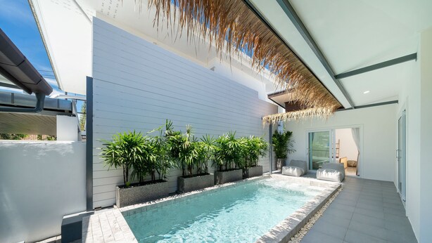 A modern outdoor swimming pool with a tiled deck, surrounded by potted plants and a thatched roof structure. - Balinese-Style 2BR Pool Villa Aemy (Rawai)