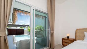 A bedroom with a large sliding glass door leading to a pool area, a bedside table with a lamp, and a bed with a headboard. - Balinese-Style 2BR Pool Villa Aemy (Rawai)