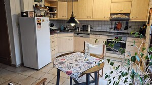 A kitchen with wooden cabinets, a refrigerator, a dining table with a patterned tablecloth, and a hanging plant. - **Charming feel-good oasis with sun terrace! Pet friendly**. (Brühl)