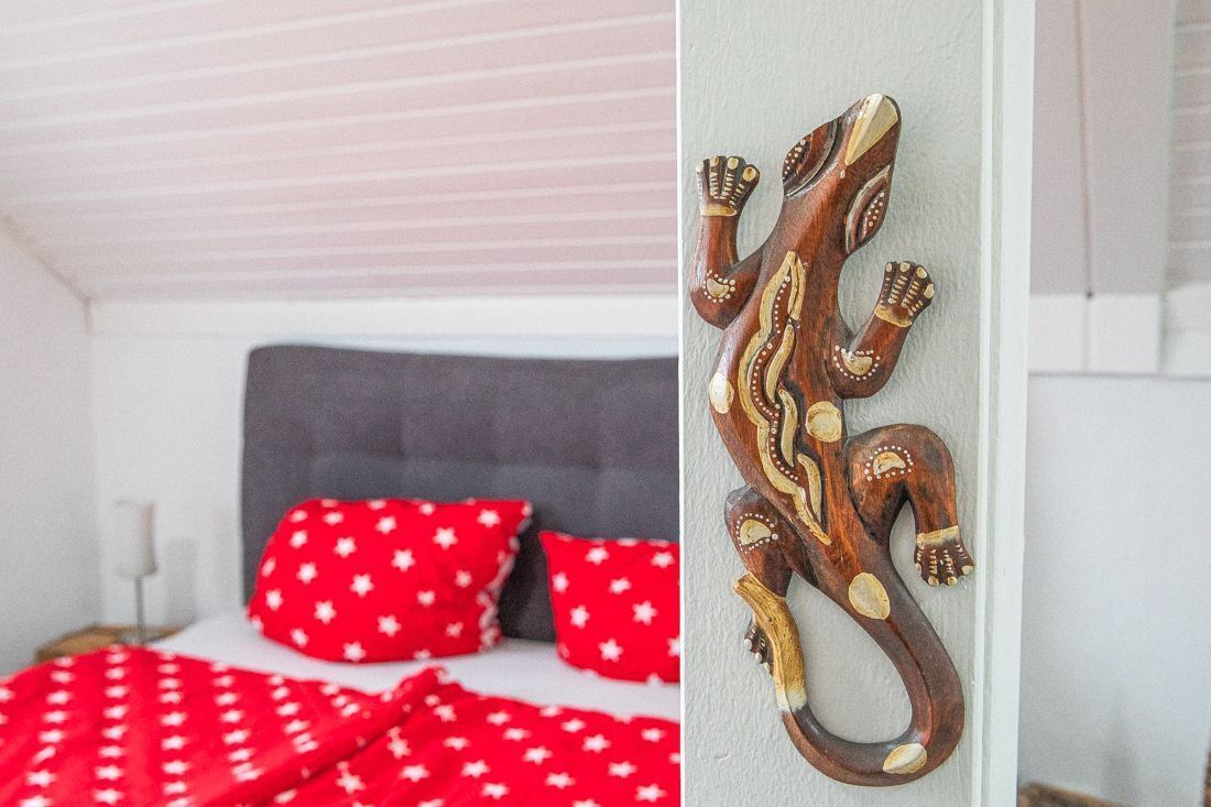 Een slaapkamer met een grijze hoofdbord, rood gestippelde lakens en een houten wanddecoratie.