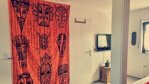 A room with a wooden door featuring tribal masks, a flat-screen TV, a small wooden side table with a plant, and a bed with a red blanket. - **Charming feel-good oasis with sun terrace! Pet friendly**. (Brühl)