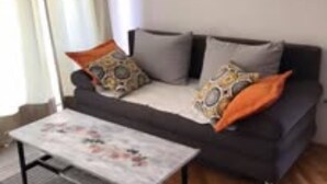 A living room with a sofa, two pillows, a coffee table, and a window with curtains. - Apartment Belu (Sibenik)