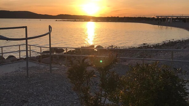A sunset over a calm body of water with a metal railing and a small plant in the foreground. - Apartment Belu (Sibenik)