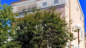 A building with a balcony, satellite dish, and a tree in front. - Apartment Belu (Sibenik)