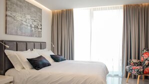 A modern bedroom with a large bed, a nightstand, a chair, and a painting on the wall. - Sunset Serenity Villa With Pool, Gym and Sauna (Kastela)