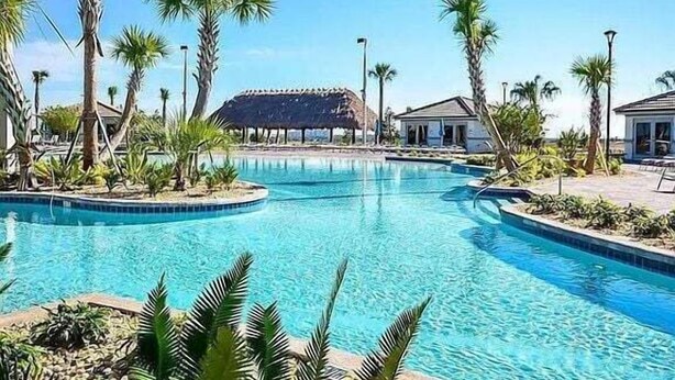 A pool surrounded by palm trees and a thatched-roof structure.