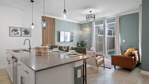 A modern kitchen with a central island, dining area, and a living space with a sofa and a view of a pool.