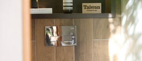 A modern bathroom with a wooden wall, a toilet, a shelf with a bottle and a sign, and a light switch.
