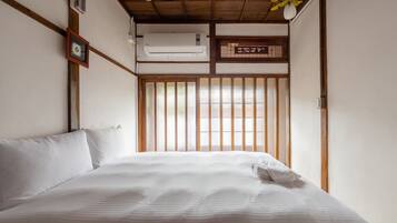 A bedroom with a bed, wooden beams, a window with vertical blinds, and an air conditioning unit.
