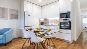 Una cocina moderna con armarios blancos, horno empotrado y mesa de comedor de vidrio con sillas.