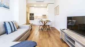En moderne stue med sofa, fjernsyn og spiseplads med bord og stole.