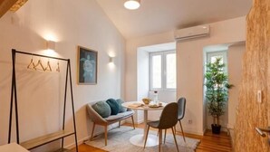 A cozy living room with a sofa, a small round table, and a chair. There is a wooden floor, a hanging light fixture, and a window with natural light.