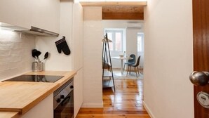 A narrow kitchen with wooden flooring, a wooden ceiling, and white walls. There is a stove, a sink, and a window in the kitchen.