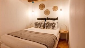A bedroom with a wooden ceiling, a bed with patterned pillows, and wall-mounted lights.