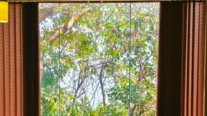 A dining area with a table set for four, surrounded by blue chairs, with a view of lush greenery through large windows. - Amritara Serenity (Sanguem)
