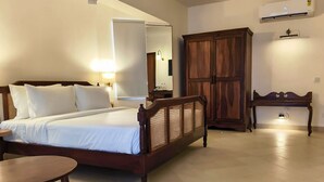 A bedroom with a wooden bed, a nightstand, a wardrobe, and a small table. - Amritara Serenity (Sanguem)