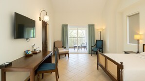 A hotel room with a bed, a desk, a chair, a television, and a balcony with a view. - Amritara Serenity (Sanguem)