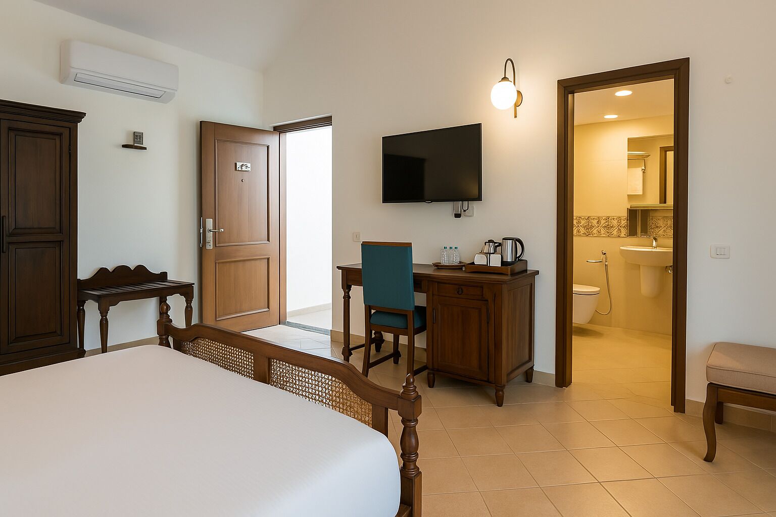 A hotel room with a bed, a desk with a chair, a television mounted on the wall, and a bathroom visible through an open door.