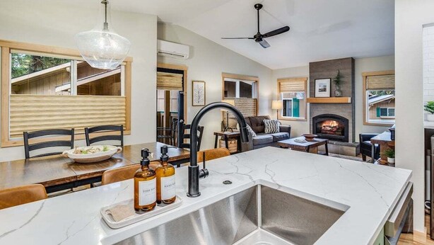 Une cuisine moderne dotée d’un grand îlot central, d’un coin repas avec des chaises en bois, d’une cheminée et d’un ventilateur de plafond.