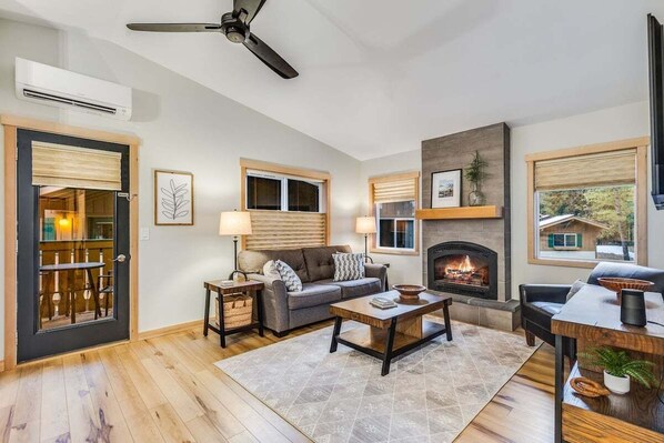 A living room with a fireplace, a ceiling fan, and a dining area with a table and chairs.