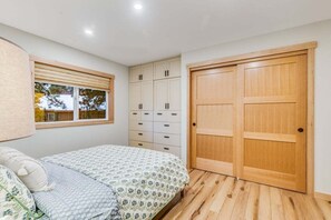 A bedroom with a bed, a window with blinds, a wardrobe, and a wooden door.