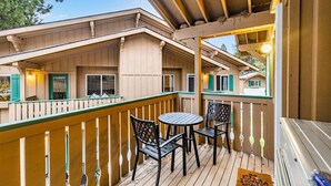 Une terrasse en bois avec une table et des chaises, un barbecue et une vue sur un immeuble doté de nombreuses fenêtres.