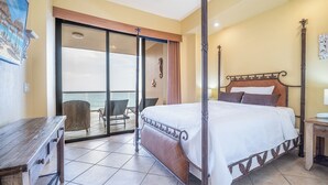 Ein Bett mit Baldachin und Holzrahmen, ein Balkon mit Korbstuhl und Blick aufs Meer.