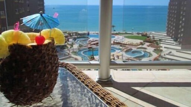 Blick von einem Balkon auf eine Küstenlandschaft mit Gebäuden, einem Pool und einem Strand.