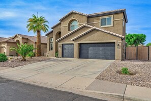 A two-story house with a garage, a driveway, and a small garden with palm trees.