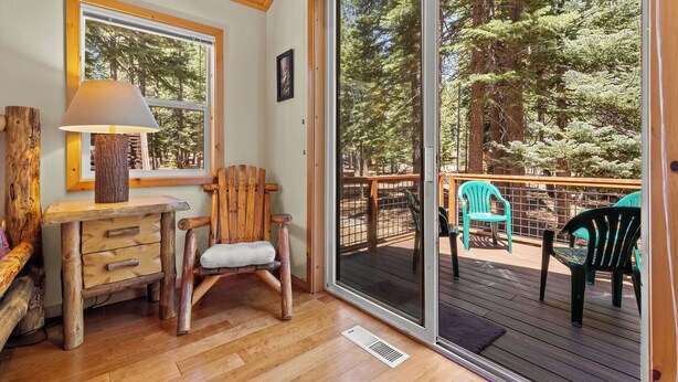 A wooden interior with a desk, chair, and a large sliding glass door leading to an outdoor deck with chairs.