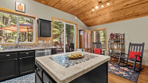 A kitchen with a granite countertop, a built-in oven, and a large window overlooking a forest.