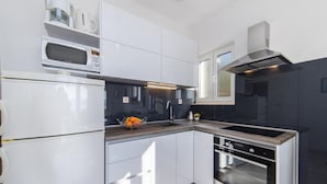 A modern kitchen with white cabinets, a built-in oven, a microwave, and a sink. - Apartment Tafra 2 (Omis)