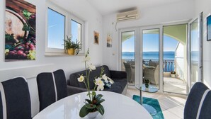 A modern living room with a view of the sea, a balcony with outdoor furniture, and a dining area with a table and chairs. - Apartment Tafra 2 (Omis)