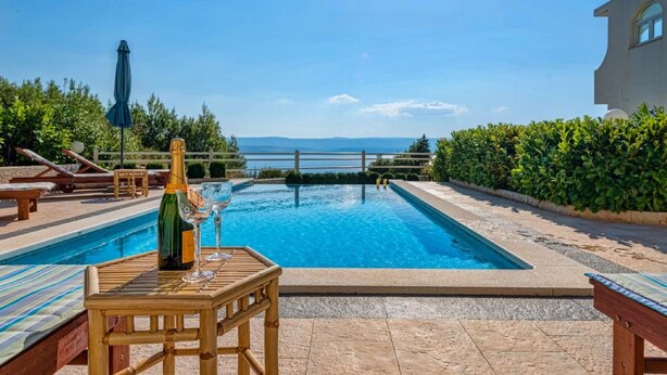 A swimming pool with a view of the sea, surrounded by lounge chairs and a table with a bottle and glasses. - Apartment Tafra 2 (Omis)