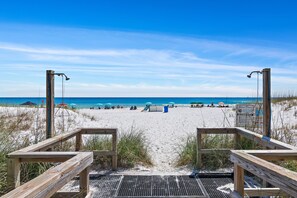 A wooden boardwalk leading to a sandy beach with umbrellas and beach chairs.