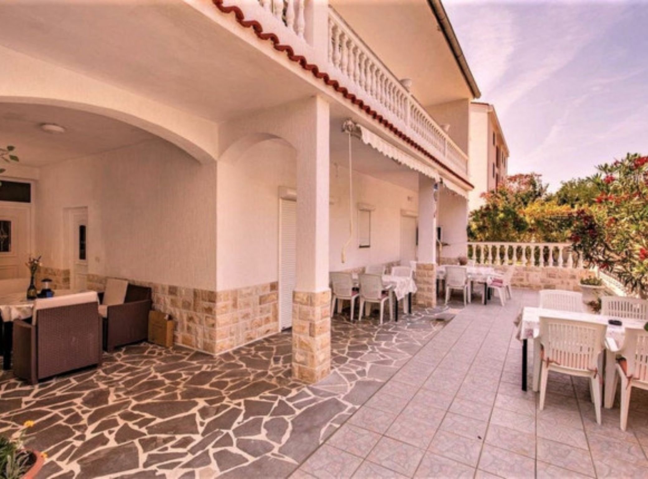 A covered outdoor area with stone flooring, white furniture, and a white fence.