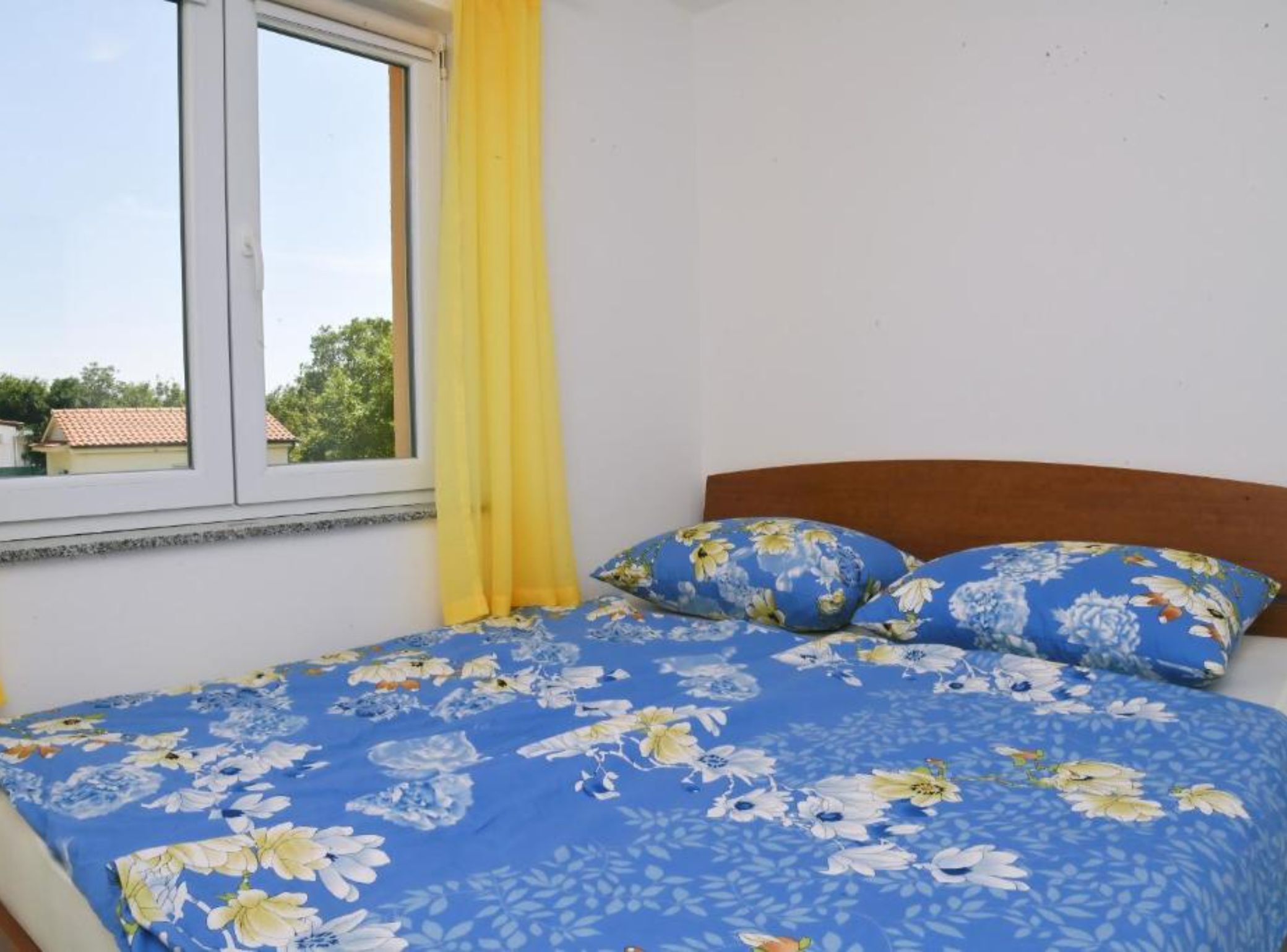 A bedroom with a bed, yellow curtains, and a window with a view of buildings and trees.