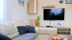 A modern living room with a sofa, a flat-screen TV, a wooden coffee table, and a small plant. - Holiday Home Mumy (Dobrinj)