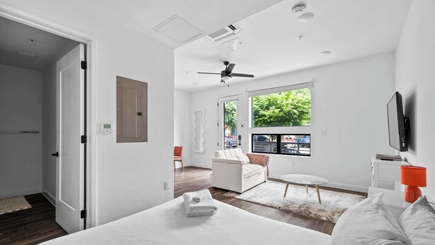 Une chambre d’hôtel moderne dotée d’un grand lit, d’un ventilateur de plafond, d’un téléviseur fixé au mur et d’une fenêtre donnant sur l’extérieur.