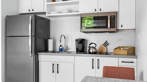 Une cuisine moderne avec des meubles blancs, un réfrigérateur en acier inoxydable, un four à micro-ondes, une machine à café et une bouilloire.