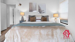 Ein Schlafzimmer mit einem Bett, zwei Nachttischlampen, einem Fenster mit Jalousien und zwei Wandbildern.