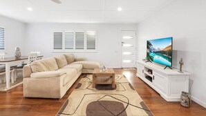 Ein modernes Wohnzimmer mit einem beigefarbenen Ecksofa, einem Holztisch und einem Flachbildfernseher auf einer weißen Unterhaltungsecke.