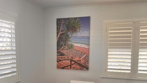 Ein Essbereich mit Holztisch, weißen Stühlen, einem Gemälde einer Strandansicht und einer Vase mit Muscheln.
