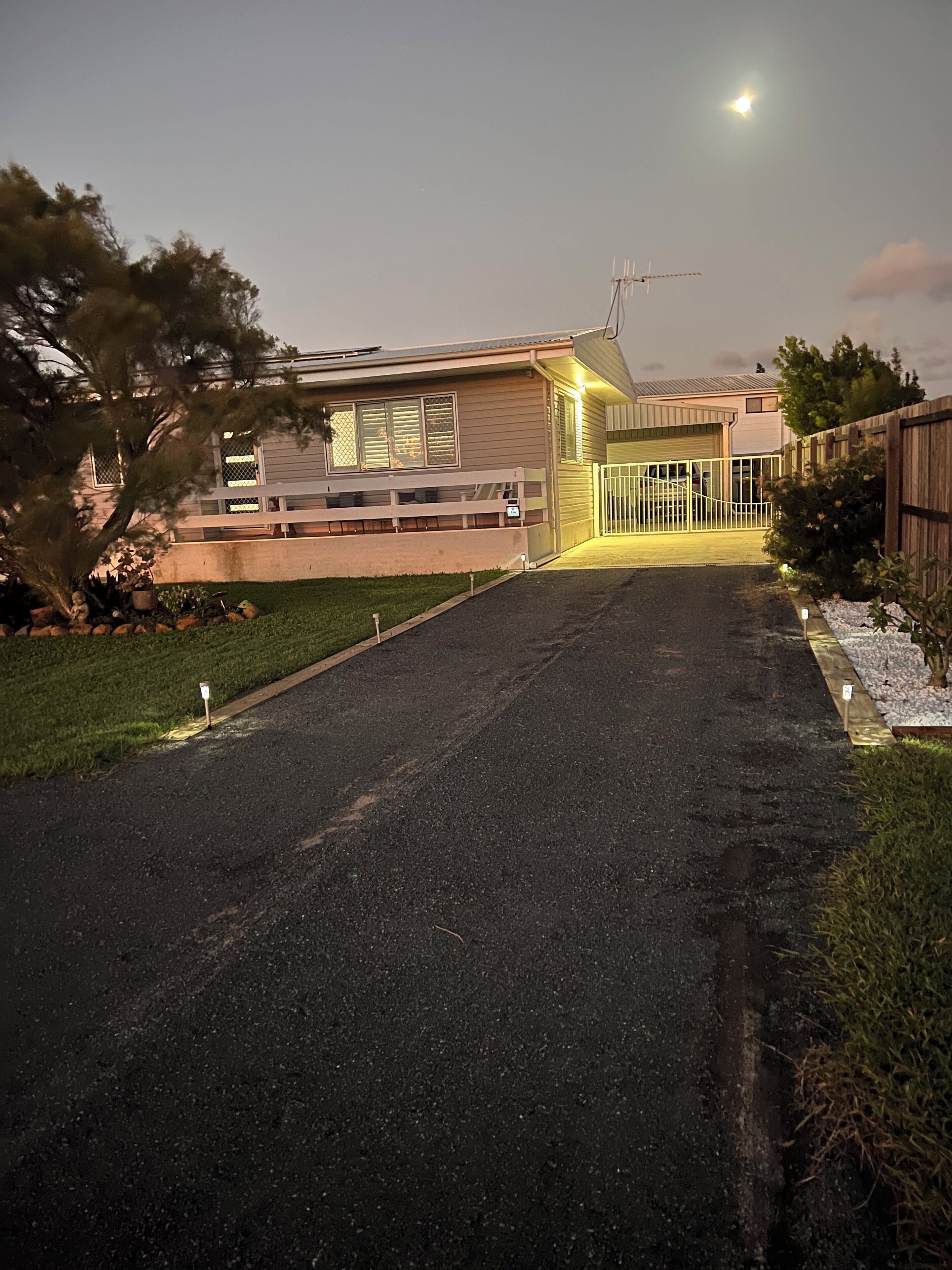 A residential driveway leading to a house with a garage, a fenced yard, and a tree on the left.